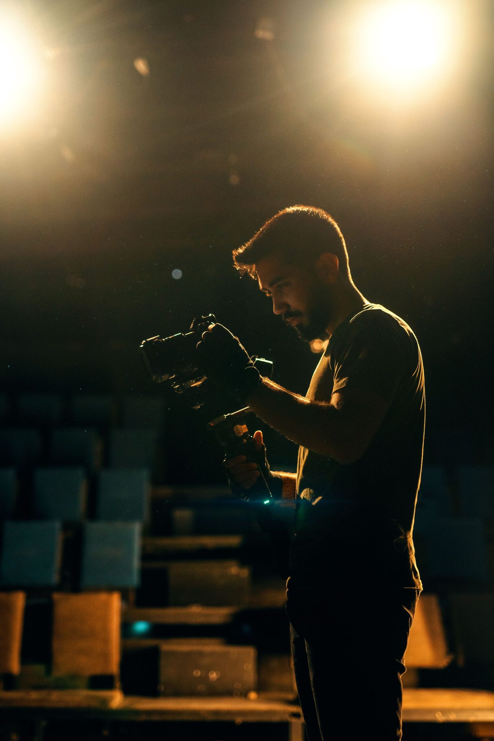A filmmaker adjusts his camera under bright stage spotlights, creating a dramatic scene.